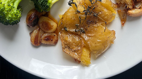 Garlic roasted baby potatoes with whole garlic cloves and thyme on a white plate